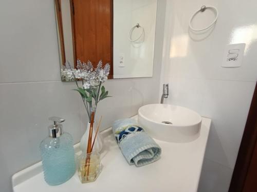 a white bathroom with a sink and a vase of flowers at Recanto da Serra in Serra Negra
