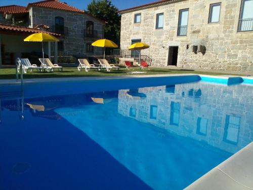 a swimming pool in front of a house with umbrellas at Quinta do Eido in Póvoa de Lanhoso
