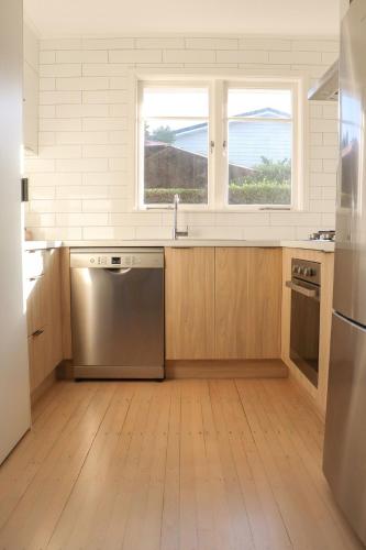 a kitchen with a stainless steel dishwasher and two windows at Beach Cottage in Mount Maunganui
