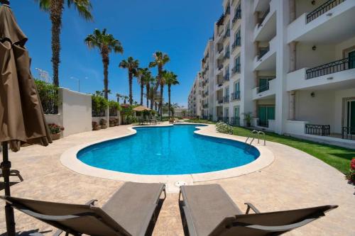 a swimming pool with two chairs and a building at Condo Paraiso - Luxurious new condo 300mt from the beach in Cabo San Lucas