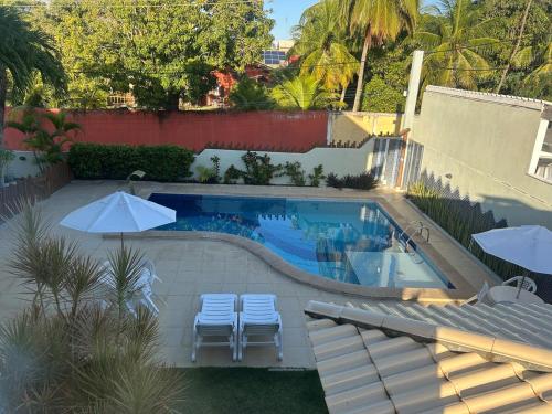 a swimming pool with two chairs and two umbrellas at Village duplex Guarajuba 3 suítes in Camacari