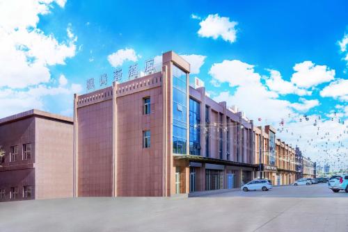 a building with cars parked in a parking lot at Yashihui Hotel in Qumul