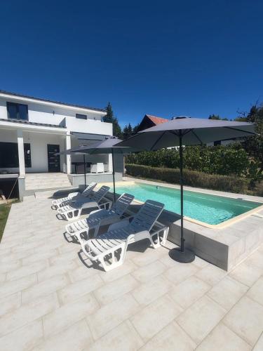 a group of lawn chairs and umbrellas next to a pool at Villa Kally in Velika Remeta