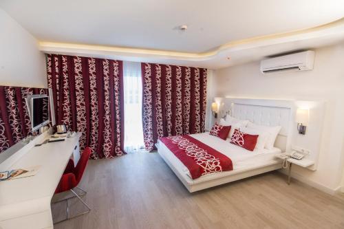 オクルカラールにあるLaguna Beach Alya Resort & Spaのベッド、デスク、カーテンが備わるホテルルームです。