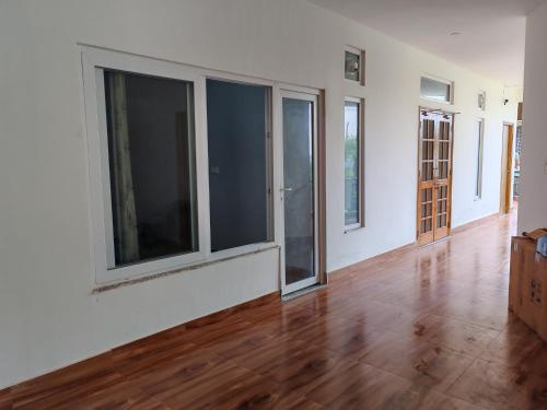 an empty living room with large windows and wooden floors at Om Homestay in Rishīkesh
