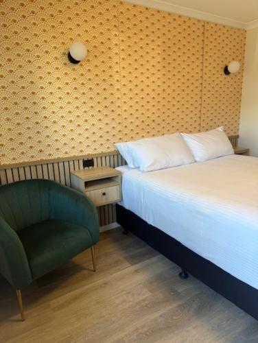 a bedroom with a bed and a green chair at The Queens Gladstone in Gladstone