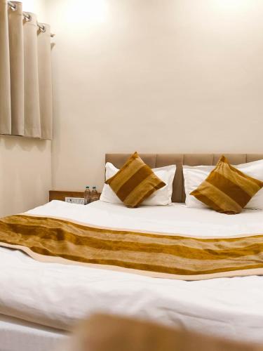 a large bed with white sheets and gold pillows at Shri ShyamRaj Hotel Ujjain in Ujjain