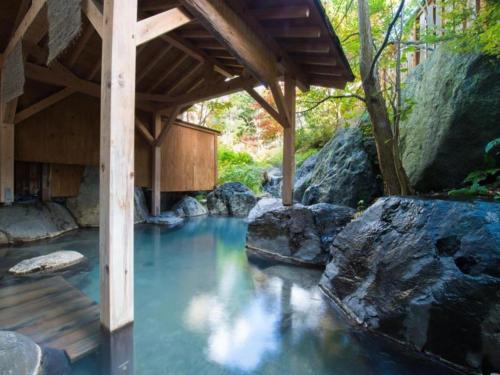 a wooden bridge over a river with rocks at Hirayu Prince Hotel in Takayama