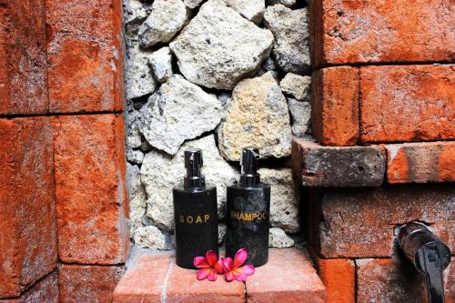 two bottles of soap sitting next to a stone wall at Umma Bali Menjangan Retreat in Banyuwedang