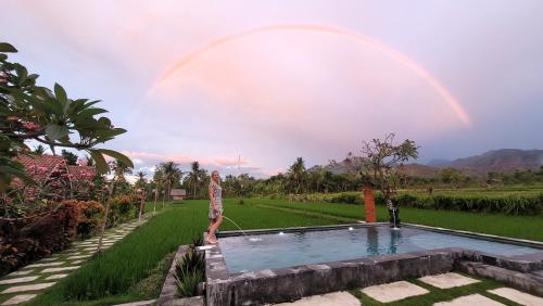 a person standing next to a pool with a rainbow in the sky at Umma Bali Menjangan Retreat in Banyuwedang