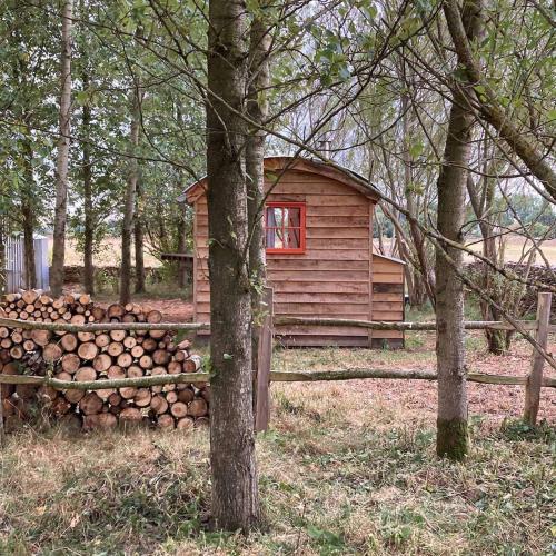 a log cabin with a pile of logs next to a pile of trees at Secluded off grid Shepherd's Hut in Minchinhampton