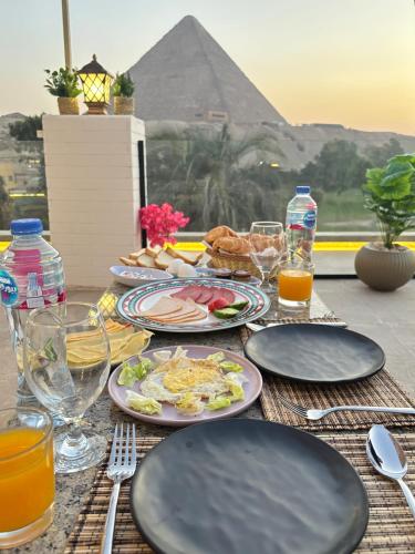 a table with plates of food and drinks and a pyramid at Beit Khufu Pyramid Hotel in Cairo