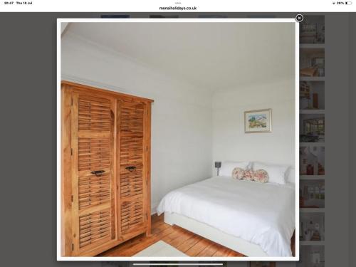 a bedroom with a white bed and a wooden cabinet at Coastal Family Escape with Castle Views in Deganwy