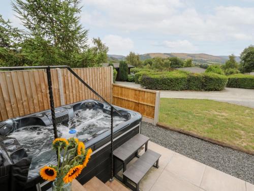 a hot tub in a garden with flowers on a patio at Dam View Shepherds Hut in Rhayader