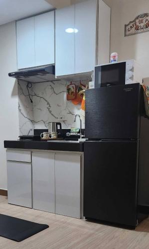 a kitchen with a black refrigerator and white cabinets at Colins Suite at Hope Residences in Trece Martires