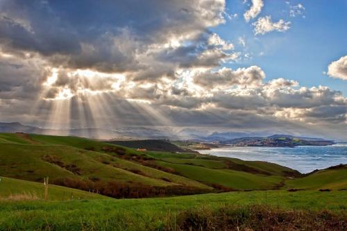 a view of the ocean and green hills with the sun shining at Casa Taro San Vicente de la Barquera in San Vicente de la Barquera