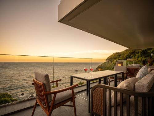 a balcony with a table and chairs overlooking the ocean at UMITO Atami Bettei in Atami