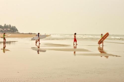 a group of people walking on the beach with surfboards at Ave Maria Guesthouse in Colva
