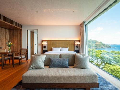 a bedroom with a bed and a couch with a large window at UMITO Atami Bettei in Atami