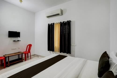 a white bedroom with a bed and a red chair at Hotel O Taaj Inn Guest House in Bhubaneshwar