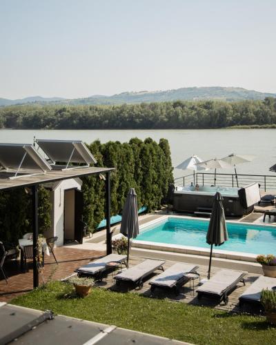 a swimming pool with chairs and umbrellas next to a lake at Guest House Panorama Aqualux with Free Parking in Novi Sad