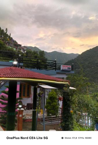 a building with a red roof with mountains in the background at Enjoy Nature at Yamuna Valley Stay in Kandi