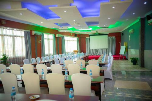 a conference room with tables and white chairs and a screen at Tiffany Diamond Hotels Ltd - Indira Gandhi street in Dar es Salaam
