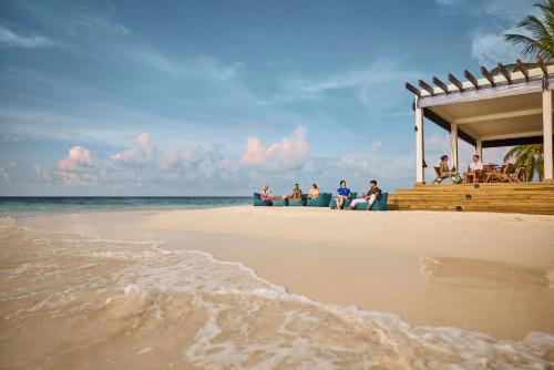 a group of people sitting on a dock on the beach at ROBINSON MALDIVES - Adults only in Gaafu Alifu Atoll