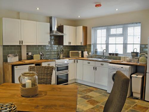 una cucina con mobili bianchi e un tavolo di legno di Elm Tree Cottage a Foxholes
