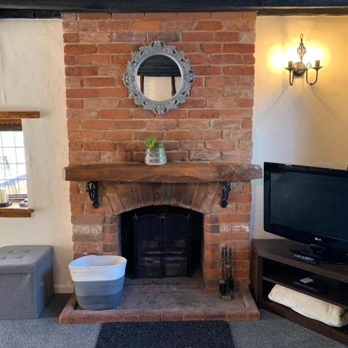 a living room with a brick fireplace with a tv at Rosemary cottage in Mountnessing