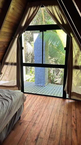 a bedroom with a large window and a wooden floor at Refúgio da natureza in São Francisco do Sul