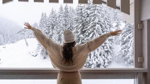 a woman looking out of a window at a snow covered forest at Ecrin Blanc Resort Courchevel - Aquapark in Courchevel