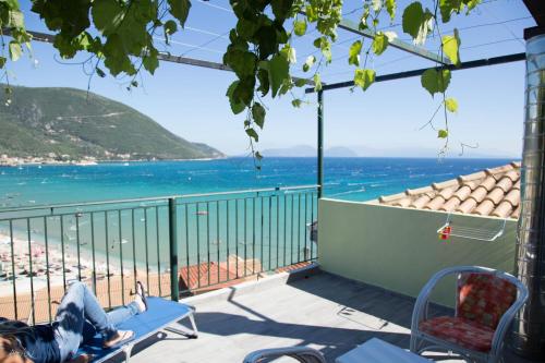 a woman sitting on a bench on a balcony overlooking the beach at Steven in Vasiliki