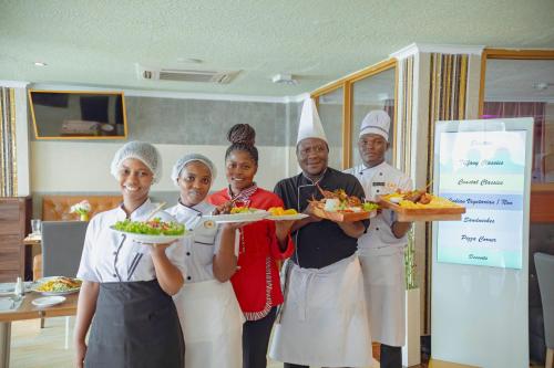a group of people standing in a kitchen holding plates of food at Tiffany Diamond Hotels LTD - Makunganya in Dar es Salaam