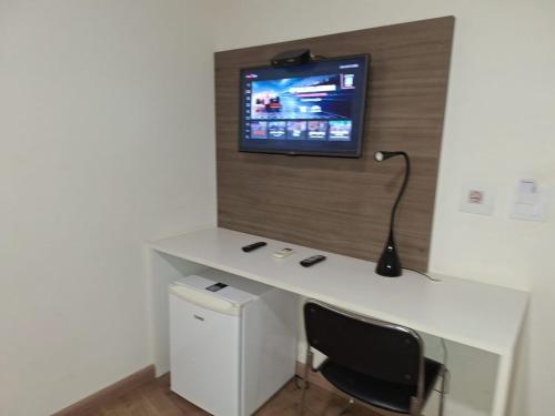 a desk with a computer and a tv on a wall at Hotel Itapema in Valinhos