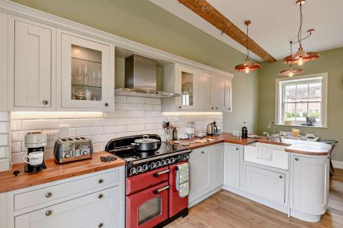 a kitchen with white cabinets and a red stove top oven at Thymblethorpe - Blythview in Blyford