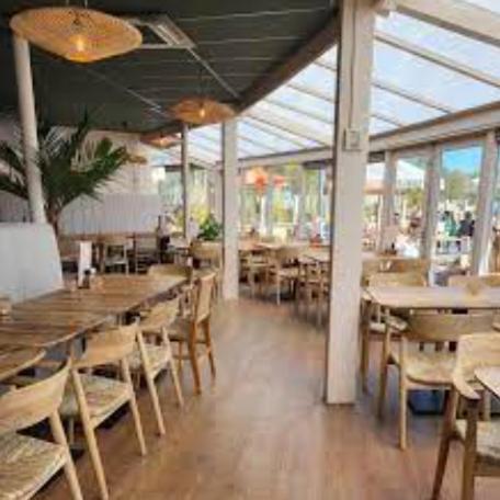 a restaurant with wooden tables and chairs and windows at Chalet Meerwijck mit Terrasse am Wasser und Meer mit Schwimmbad in Kropswolde