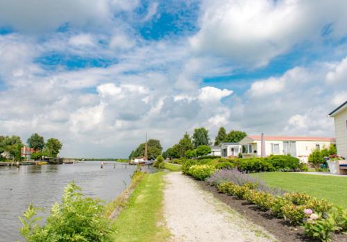 a path next to a river with a house at Chalet Meerwijck mit Terrasse am Wasser und Meer mit Schwimmbad in Kropswolde
