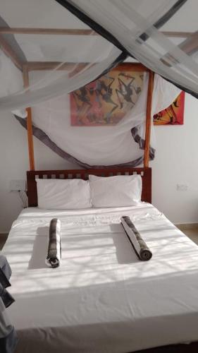 a bedroom with a white bed with two remote controls on it at Kijani unique home Malindi in Malindi