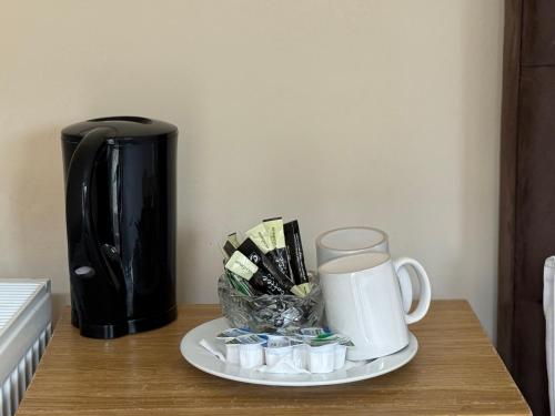 a coffee maker and a plate with a cup on a table at Airport Guest House in Slough