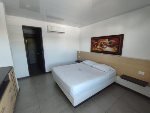 a bedroom with a white bed and a painting on the wall at Hotel Agua Azul Melgar Tolima in Melgar