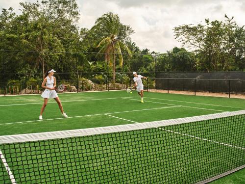 two people playing tennis on a tennis court at Etéreo, Auberge Collection in Playa del Carmen
