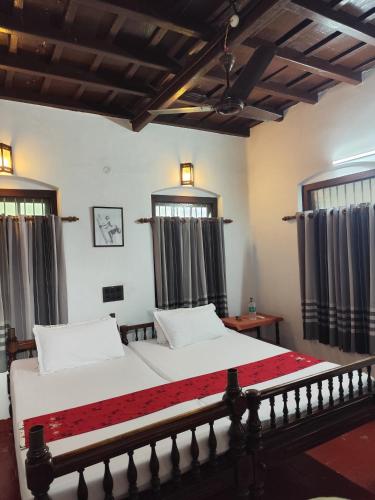 a bedroom with a bed with white sheets and windows at Alleppey Tharavad in Alleppey