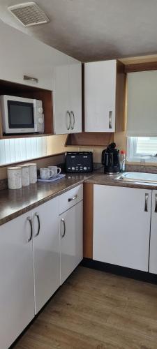 a kitchen with white cabinets and a microwave at Willerby Delux - Holiday Home by the Sea - close to the Entertainment Complex-bedding, towels & wifi Included! in Jaywick Sands