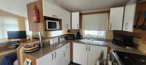 a small kitchen with white cabinets and a microwave at Willerby Delux - Holiday Home by the Sea - close to the Entertainment Complex-bedding, towels & wifi Included! in Jaywick Sands