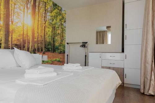 a bedroom with a white bed with a forest view at Просторен апартамент за семейна почивка in Hisarya