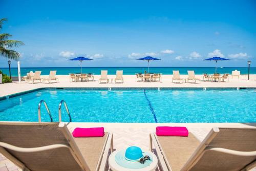a swimming pool with chairs and umbrellas and the ocean at Georgetown Villas #113 in Seven Mile Beach