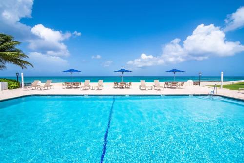 a swimming pool with chairs and umbrellas and the ocean at Georgetown Villas #218 in George Town