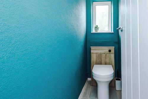 a blue bathroom with a toilet and a window at 3BR House By Eason Stays Short Term Rental Wythenshawe Near Manchester Airport with Free Parking in Wythenshawe
