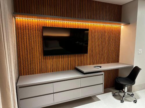 a tv on a wall with a desk and a chair at Apartamentos Exclusivos no Edifício City House in Barreiras